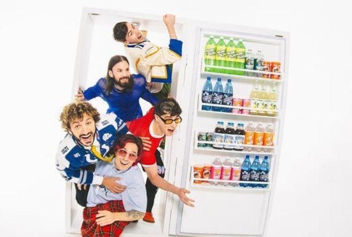 Members of the band Good Kid playfully posing as if climbing out of a fridge stocked with colorful beverages.