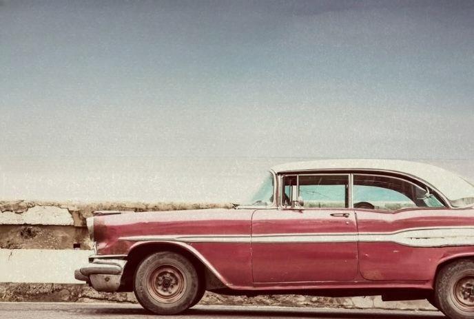 A vintage red car with a white roof is parked beside a weathered stone wall.