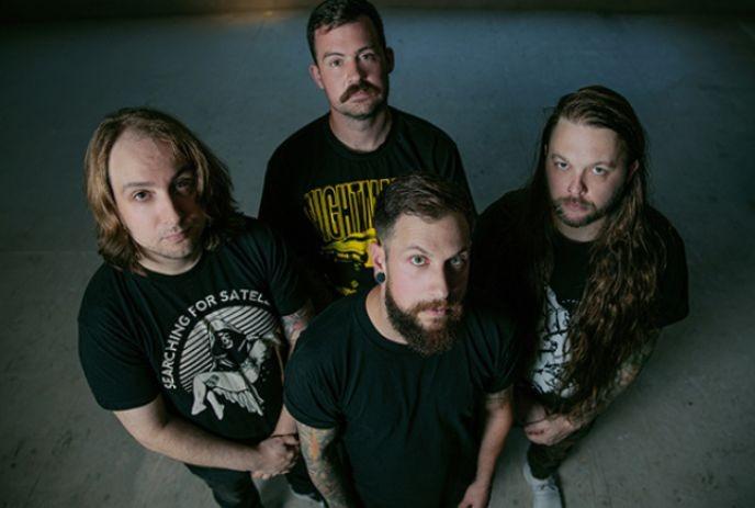 Four men of the band Dead Days stand together in dim lighting, gazing up.