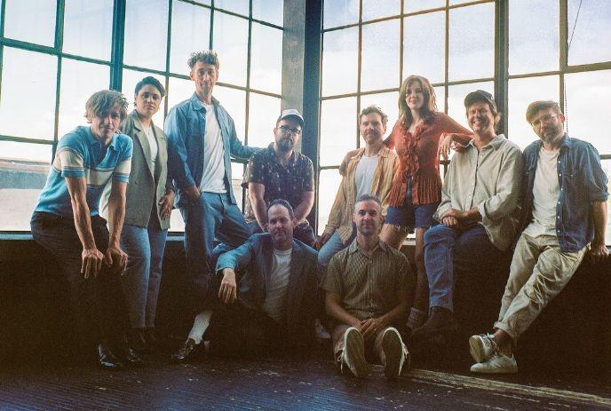 The ten members of Dwayne Gretzky posing casually in front of large windows, with natural light creating a warm, relaxed atmosphere.