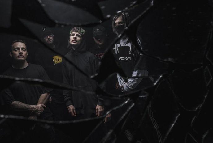 5 band members of Alpha Wolf stand in dark clothing, viewed through shattered glass.
