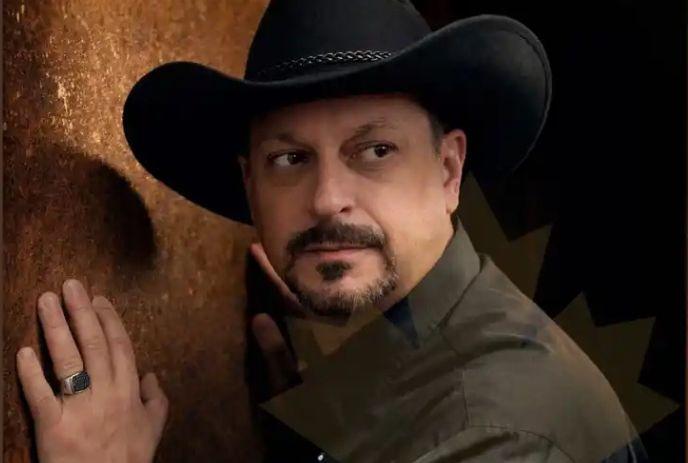 Savvy Savoy with a hand on a wall, looking to the side and wearing a black cowboy hat.