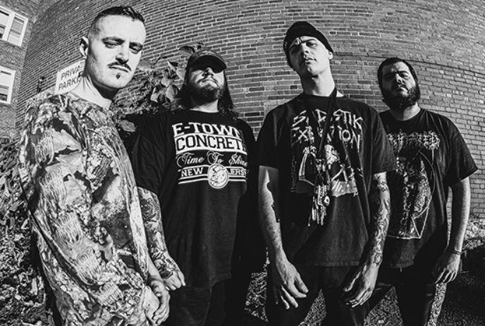 Four men of the band The Last Ten Seconds Of Life stand in front of a brick wall, wearing dark graphic tees.