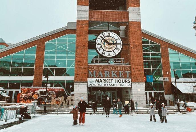 People skate in front of Covent Garden Market, a red-brick building with large glass windows.