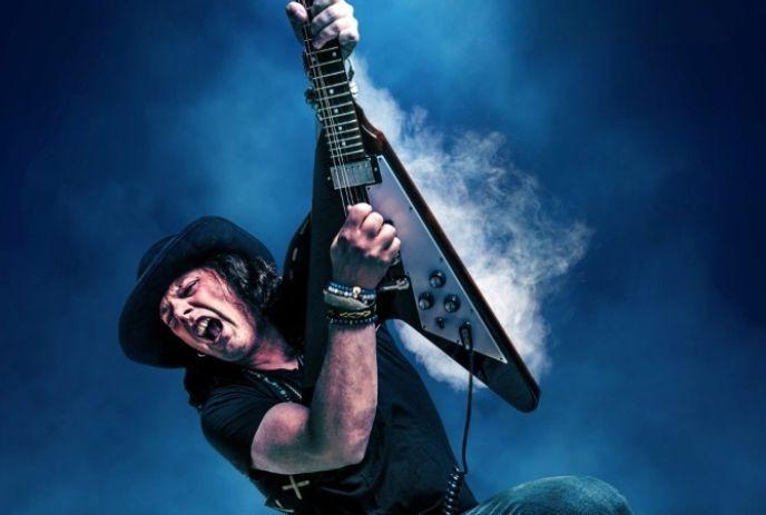 Anthony Gomes passionately plays an electric guitar onstage, surrounded by wisps of smoke.