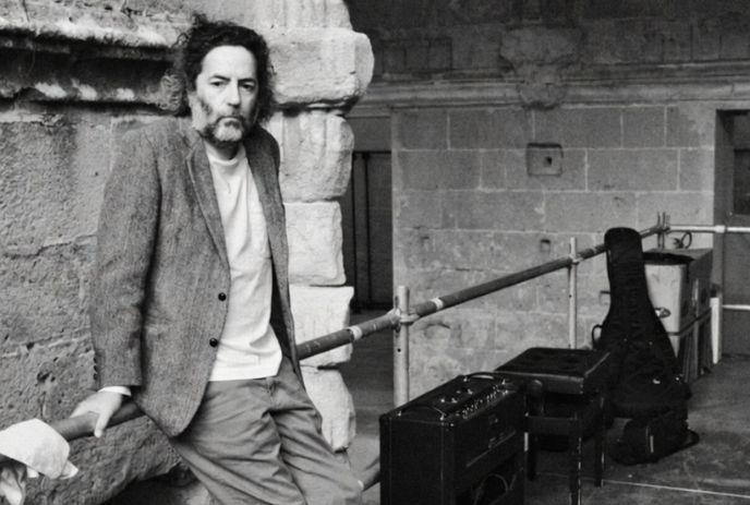 Destroyer leaning on stone wall in a rustic setting, wearing a blazer and t-shirt.