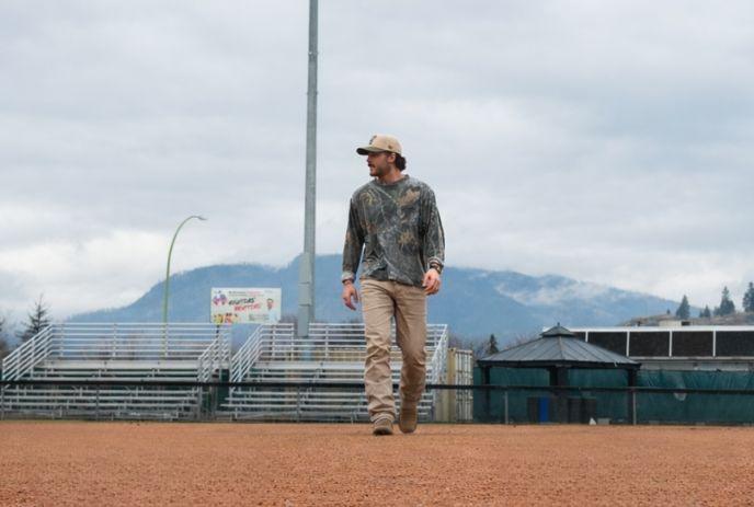 Dawson Gray in a shirt and beige pants walks across an empty baseball field.