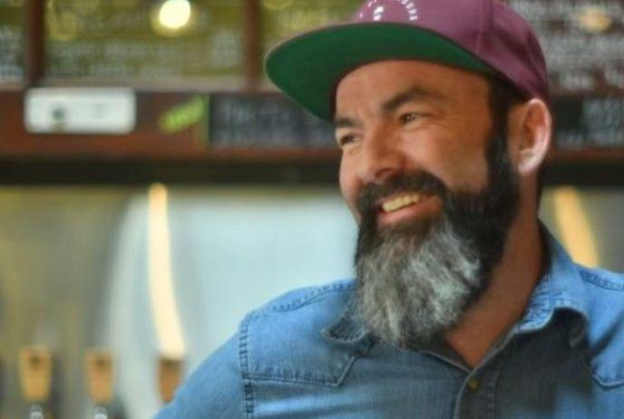 Jim MacDonald wearing a green and purple flat-brimmed hat, smiling while indoors.