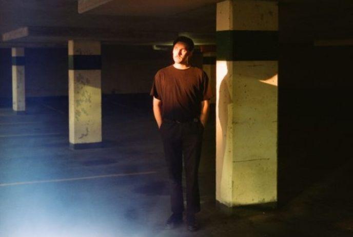 Willem James Cowan standing with his hands in his pockets, in an underground parking garage with no cars.
