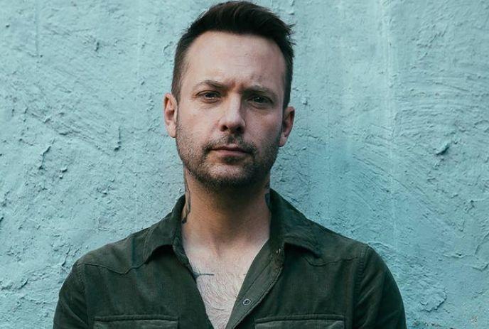 Dallas Smith posing for the camera expressionless, against a greyish wall.