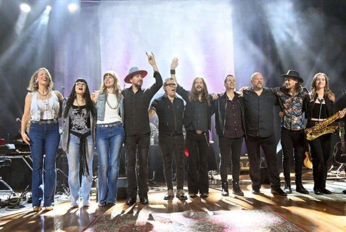 Forever Seger, a Bob Seger tribute band, poses arm-in-arm on stage, smiling and waving under purple lights.