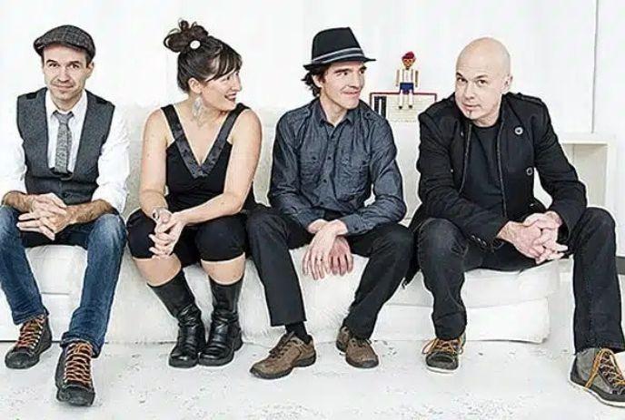 The four band members of Melisande sitting on a white couch in a white room, posing for the camera.
