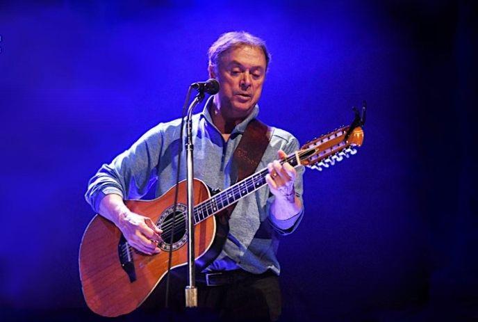 Cliff Erickson performing on stage with a guitar in front of a blue background.