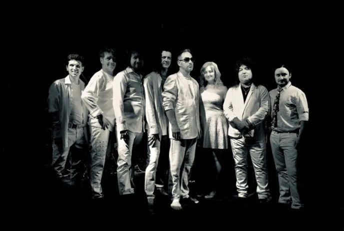 A black and white photo of the 8 performers of Dreamer: The Supertramp Experience, posing for the camera in front of a black background.