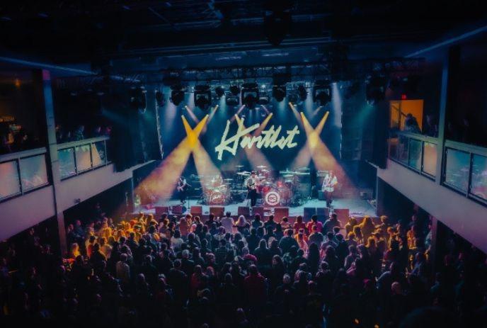 Hartlet performing on stage in front of a crowd, with their band name on the stage screen.