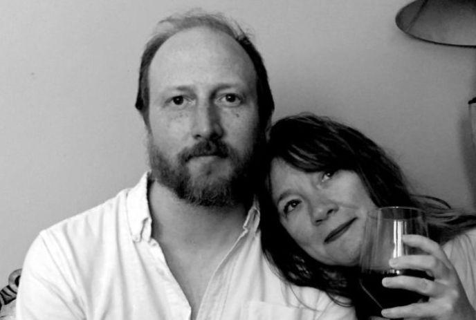 A black and white photo of Colleen & Steve Murphy, with Colleen resting her head on Steve's shoulder, holding a wine glass.