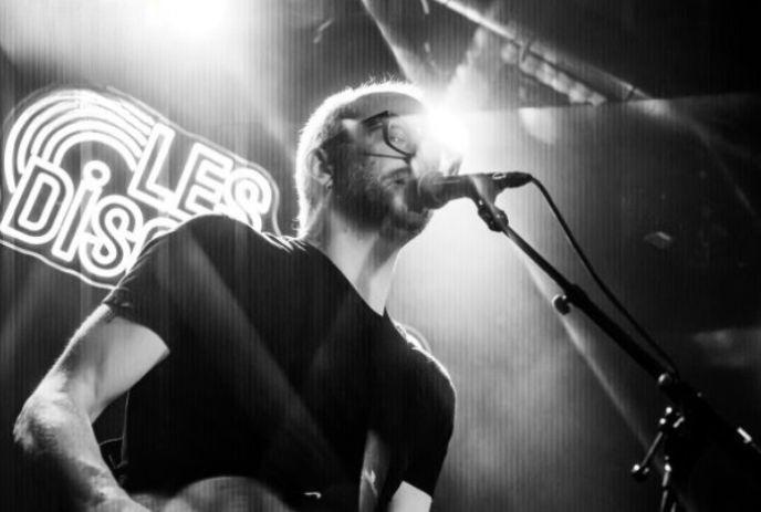 A black and white photo of Eric Howden singing on stage with a guitar.