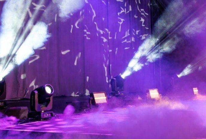 A talent show stage shrouded in purple smoke with beaming spotlights and patterned curtains.