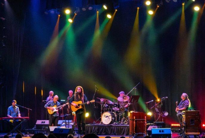 A group of musicians performing on stage under colourful spotlights.