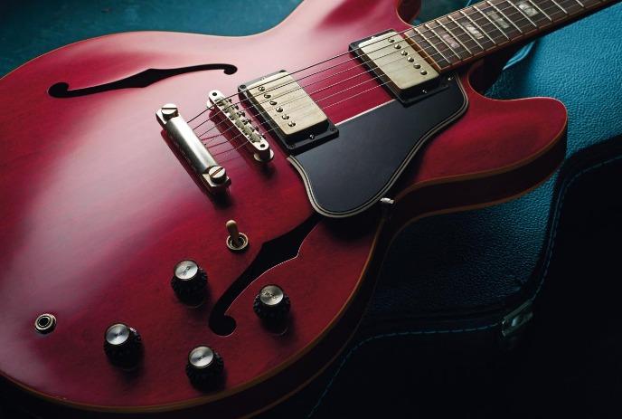 Red electric guitar on blue case with pickups and knobs.