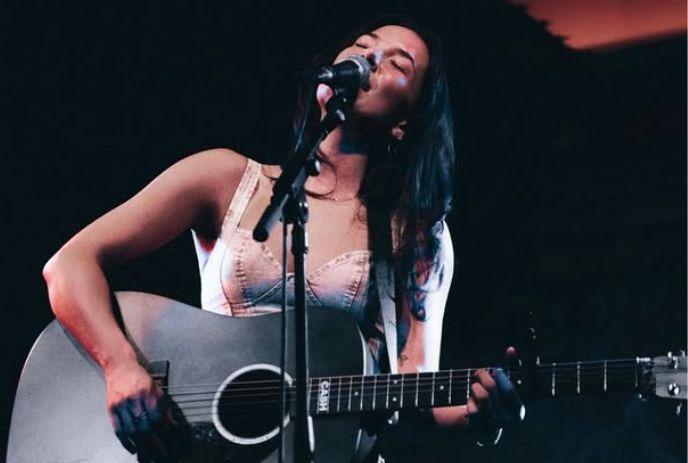 Jimi on a stage with her guitar, singing with her eyes closed.