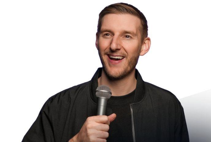 Jeremiah Watkins portrait, smiling warmly with a microphone in hand, before a white background.