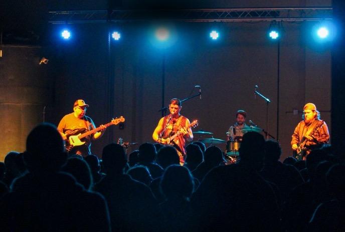 Four band members on stage with their instruments.