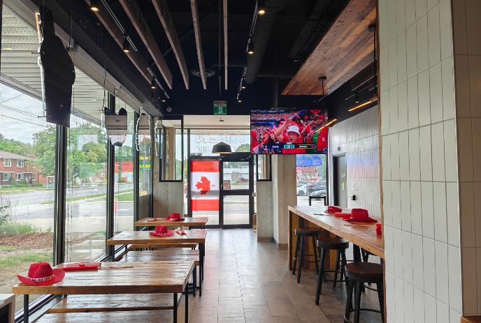 Modern café with wooden tables red hats glass windows Canadian flag and TV showing sports fans in bright space.
