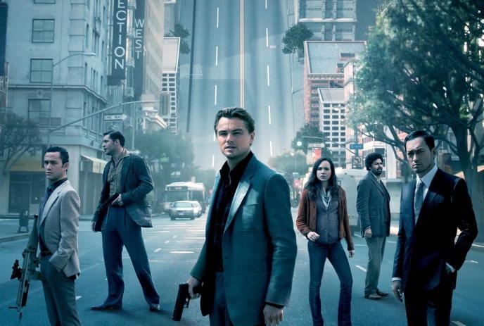 Six people in suites and wielding weapons stand in a city street, with buildings and road behind them.