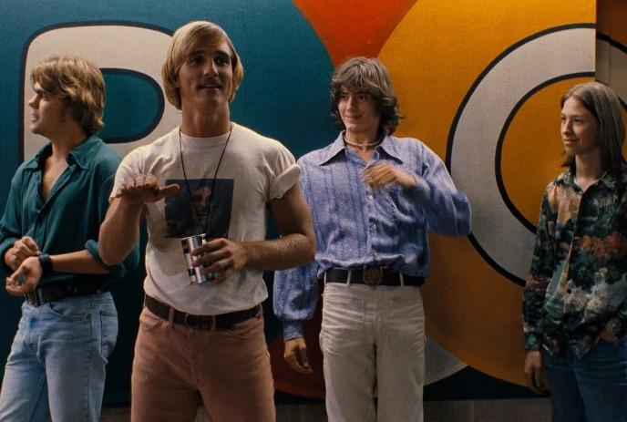 Four young men stand chatting before a bright mural of bold circles in warm retro tones.