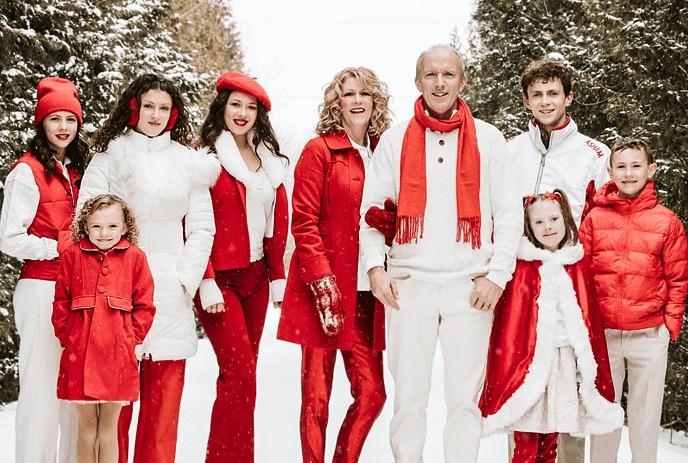 Snowy path family portrait in red and white winter outfits among greens creating a festive seasonal scene.