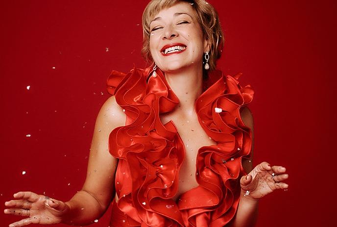 Singer in a vivid red gown performs before an orchestra as the conductor leads a vibrant concert.