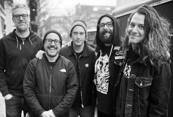 A black and white photo of the 5 members of A Wilhelm Scream posing outside in a city, smiling.