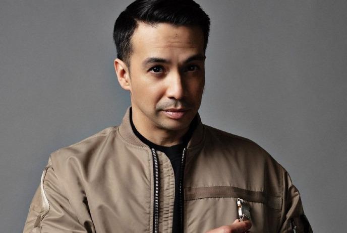 Laidback Luke looking at the camera, wearing a tan jacket in front of a grey background.