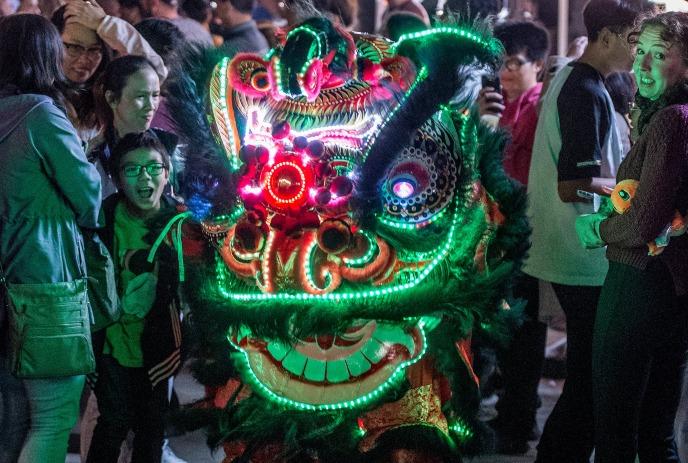 A glowing dragon costume dazzles the crowd, bathed in vibrant festival lights, alive with energy and celebration!