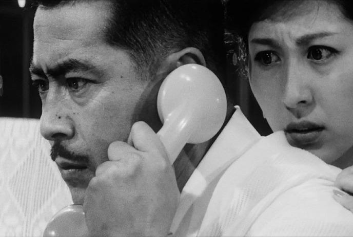Person holds telephone near ear; black and white tones with a lady on the back.