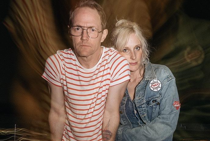 Whitehorse in a striped shirt and Chloe Doucet in a denim jacket stand closely, looking forward.