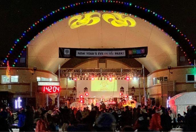 Crowd gathers at lit stage for New Year’s Eve in the Victoria park, celebrating with music and festive lights.