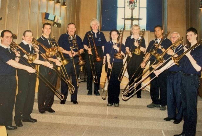 Ten trombonists in navy shirts pose on steps indoors posing for a picture.