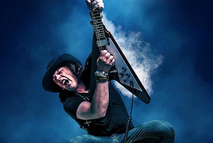 Anthony Gomes passionately plays an electric guitar onstage, surrounded by wisps of smoke.