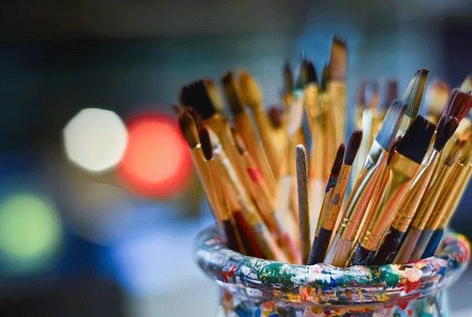 A bunch of used paint brushes in a glass holder.