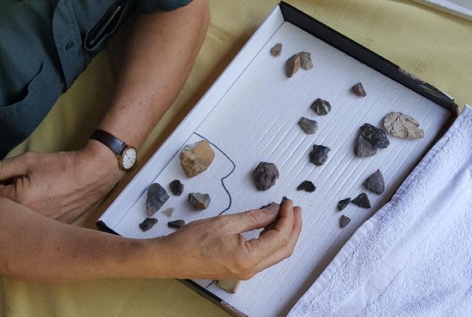 A person examines stones in a box; rocks lie on a white surface, one held between their fingers with focus.