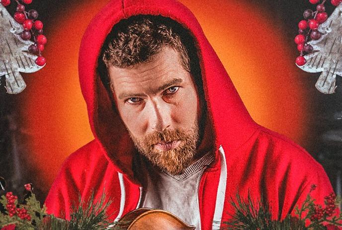 Artist in a red hoodie, holding a violin amid festive holiday greenery and decorations.