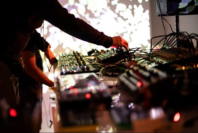 A dj at a sound  table, with colourful lights in the background.