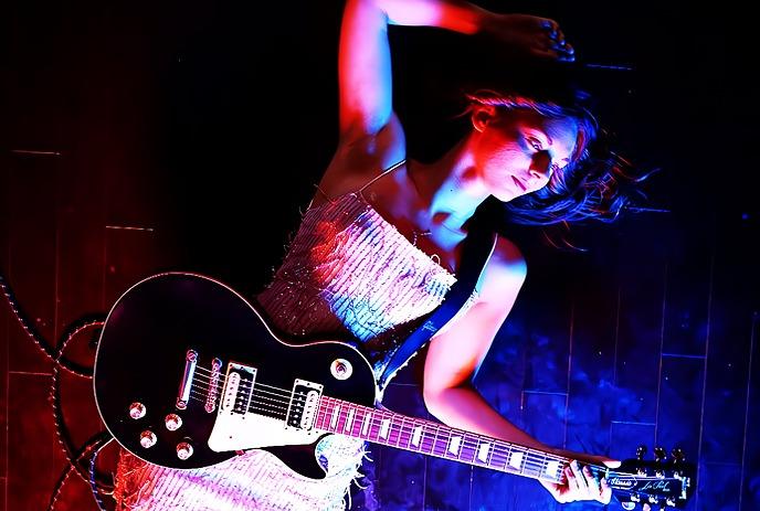 A woman lying on her back on the ground with a guitar, illuminated by red and blue light.