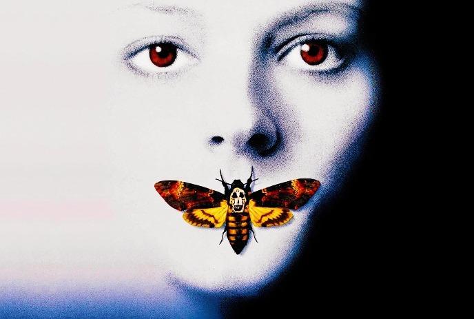 Pale face with red eyes close up as large moth covers mouth its bright wings forming eerie silent motif.