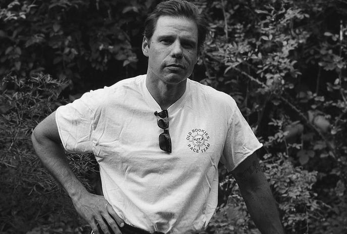 A cyclist in a helmet rides a bicycle against a yellow background with horizontal stripes.