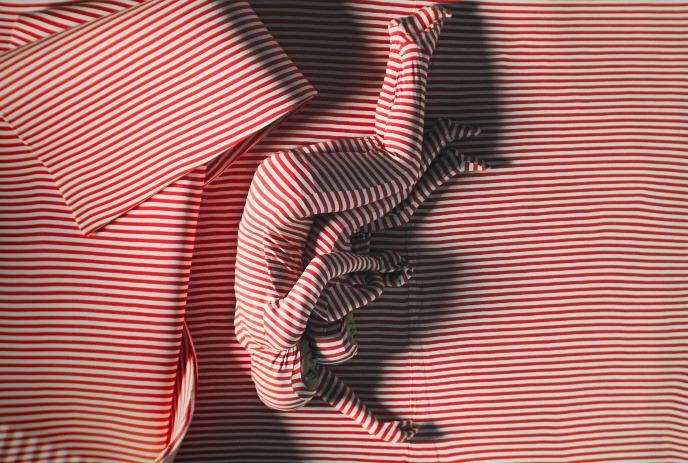Figures lying on striped bed blending into matching red, white pattern.