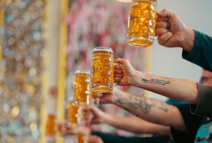 Cheers with beer mugs raised high in Oktober fall festival under a blurry background.