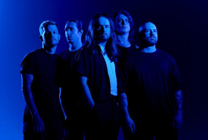 Five band members of Fit for a King stand in a dramatic blue-lit setting, each with serious expressions.